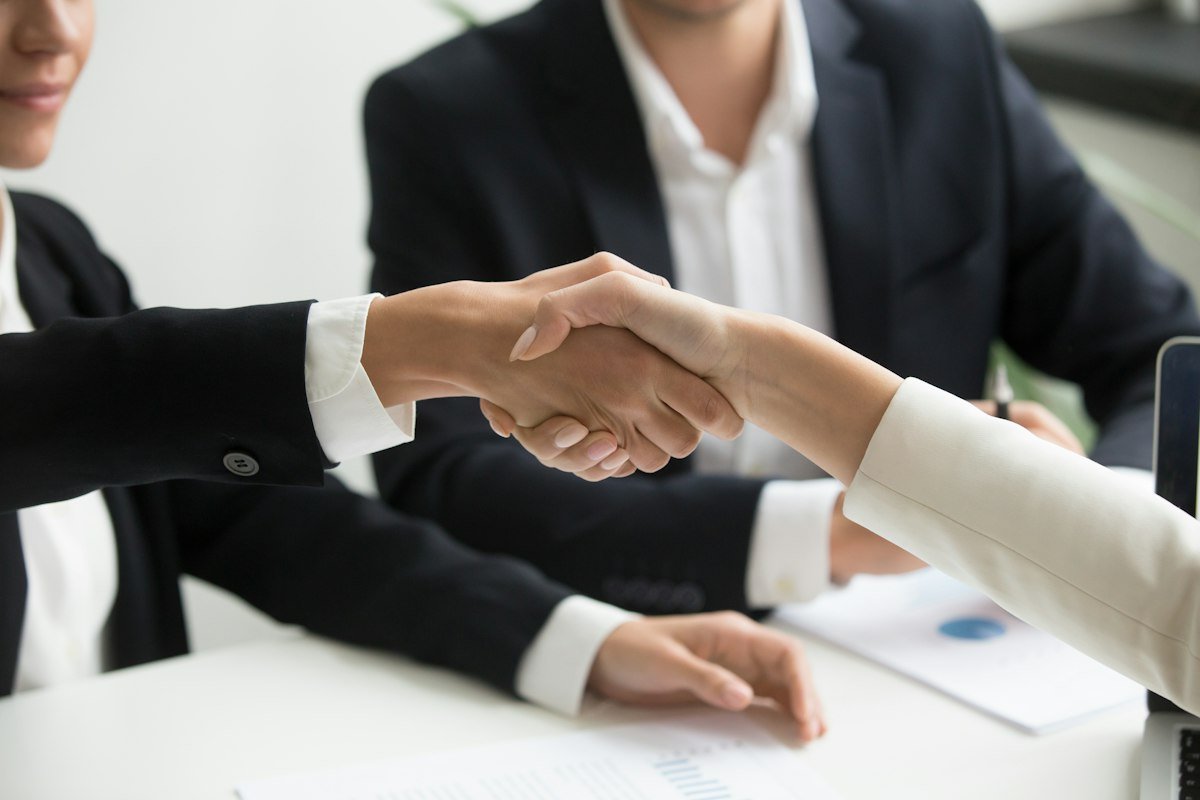 Two people shaking hands in front of a laptop