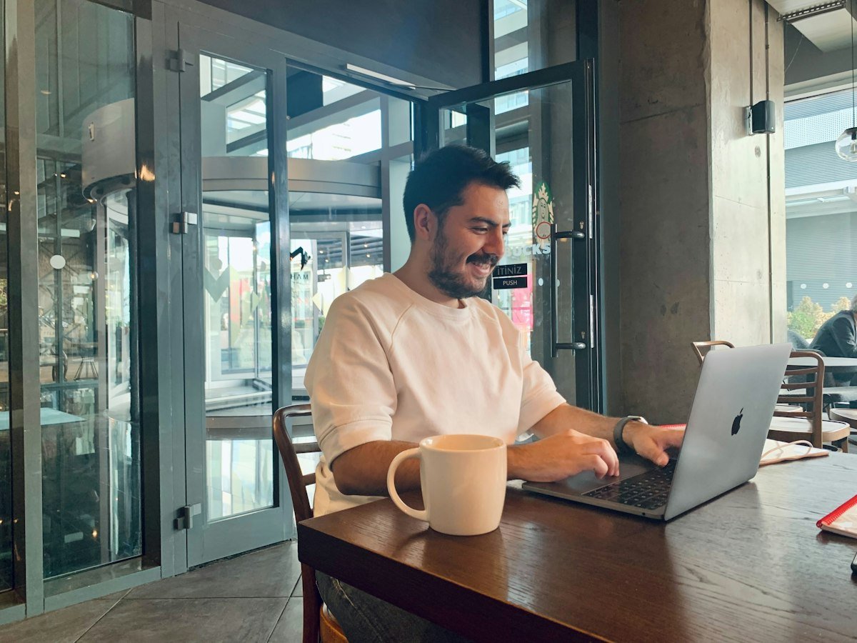 A man smiling while working on a laptop in a cafe